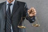 male-lawyer-s-hand-showing-justice-scale-against-gray-textured-b