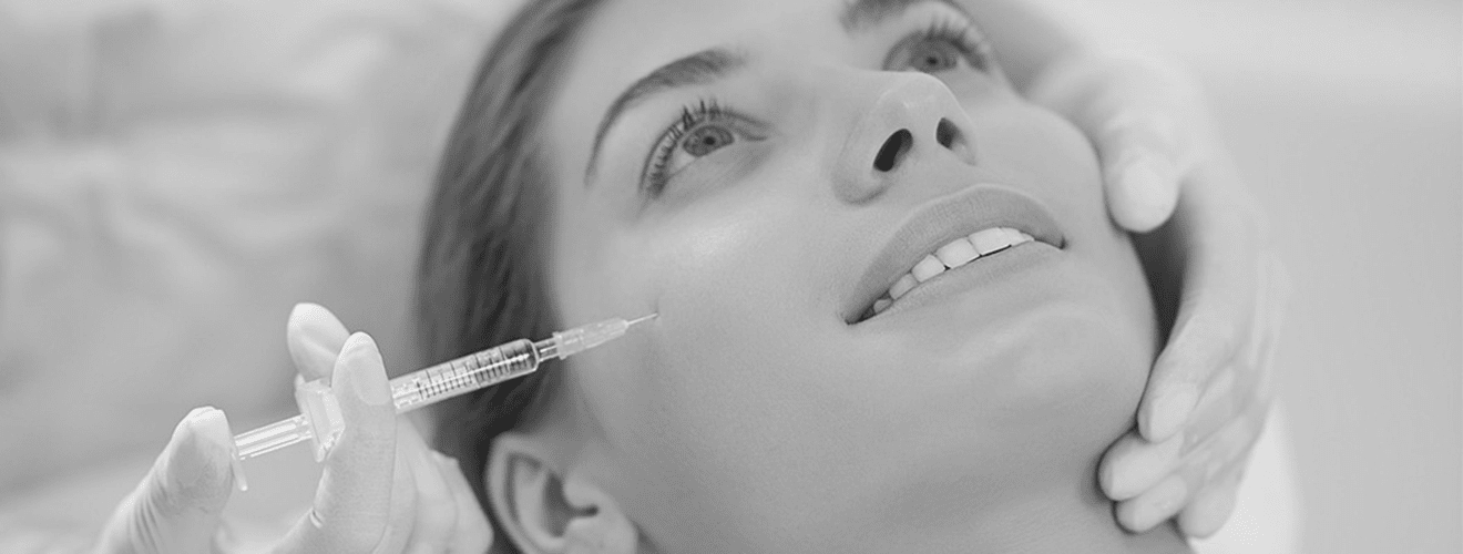 Woman receiving a dermal filler (Hyaluronic Acid) injection in the cheekbone area for facial volumization.