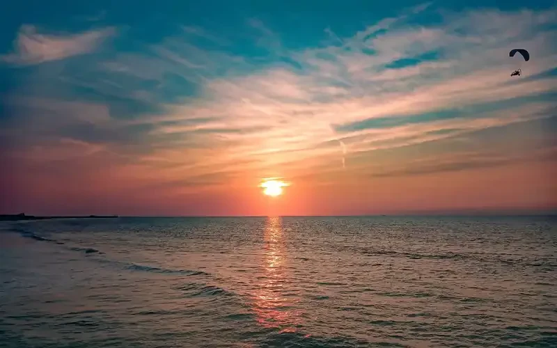 Gün batımında kıyının üzerinde süzülen yamaç paraşütçüsü
