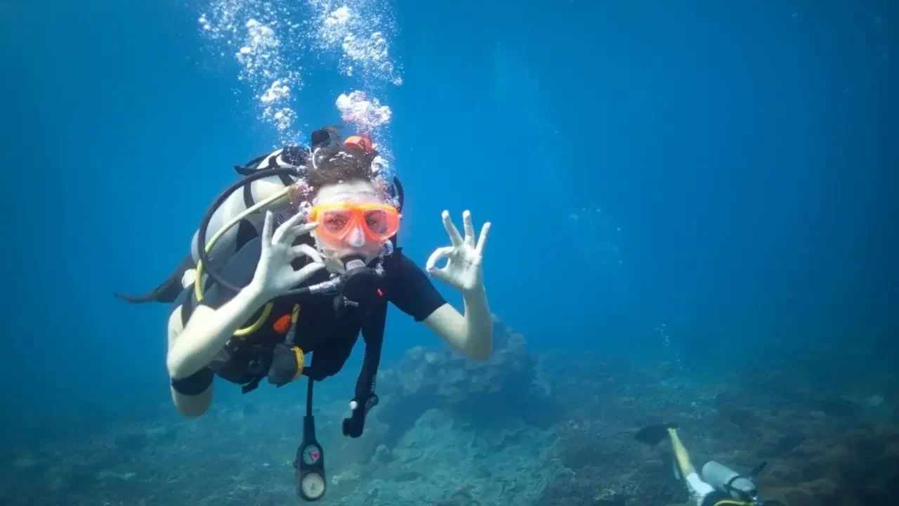 Diver with a red mask giving the OK sign underwater