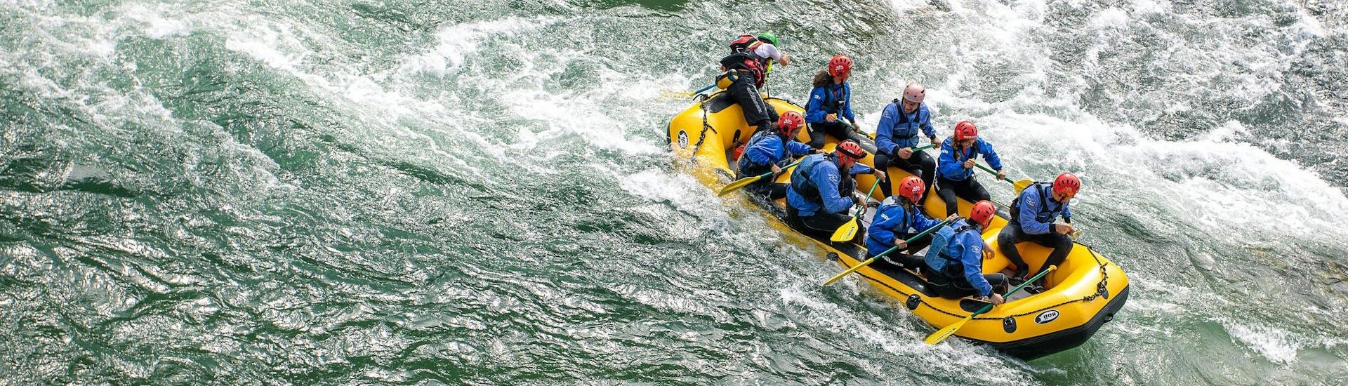Hızlı akan bir nehirde sarı bir botla rafting yapan, kask takmış ve kürek çeken bir macera grubu
